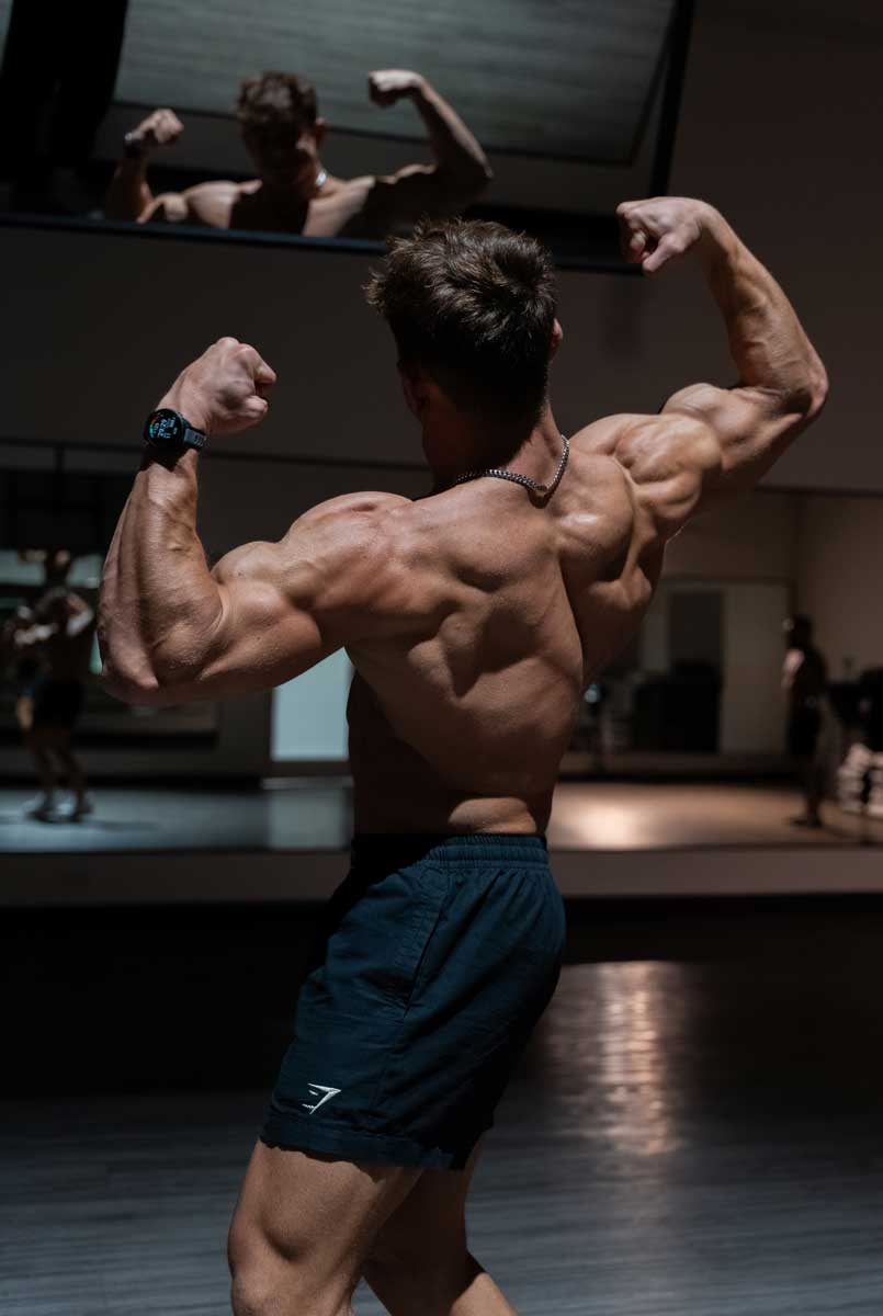 The coach is back posing to show his back muscle.